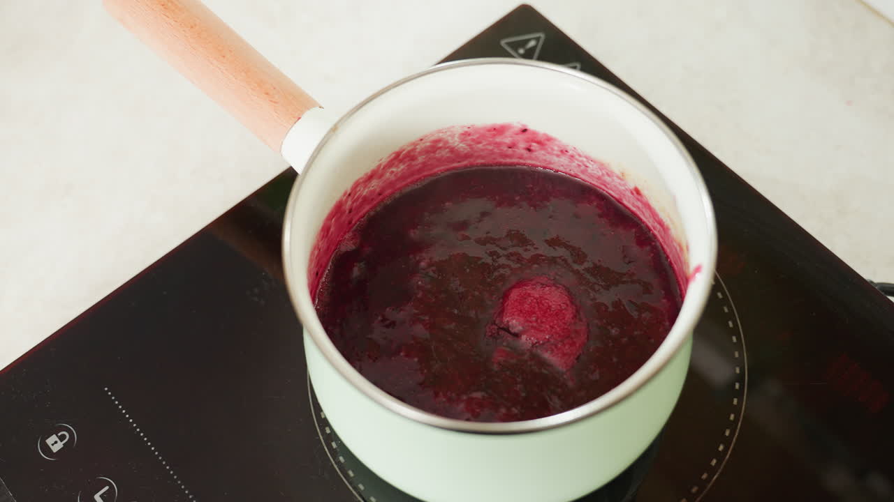 Close up of thick red soup or sauce bubbling gently in pastel green pot on electric stove, highlighting texture, heat activity, and rich color during home cooking process in clean kitchen environment