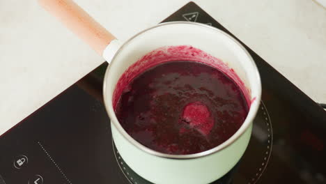 close up of thick red soup or sauce bubbling gently in pastel green pot on electric stove, highlighting texture, heat activity, and rich color during home cooking process in clean kitchen environment