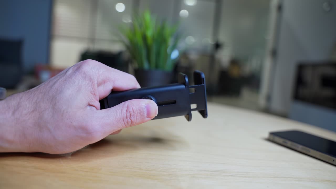 Close-up of a hand holding a clamp mount over a wooden desk in a modern workspace. Ideal for tech, setup, tutorial, or productivity scenes.