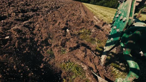 tractor plowing field with fresh soil turning over in sunlight