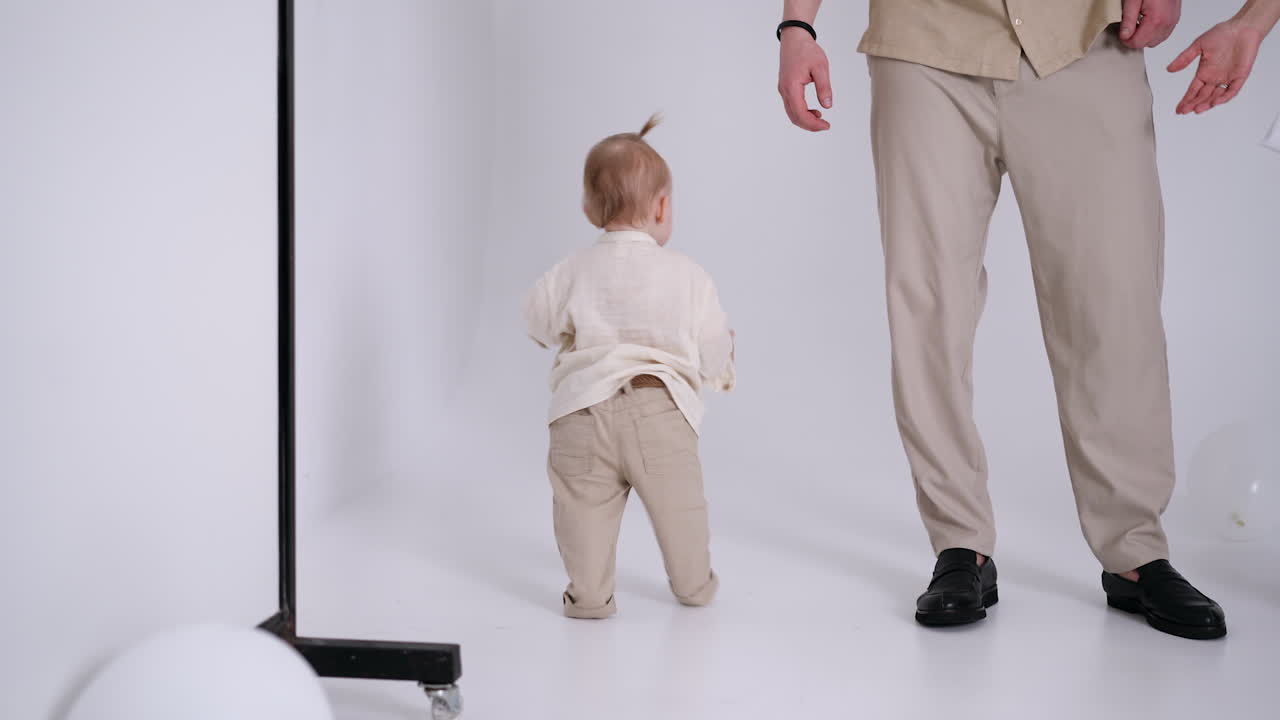 Adorable little baby walking by the photo studio. Unrecognized parents are beside their child.
