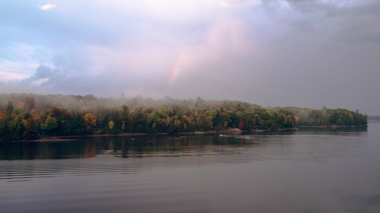 paso elevado del lago con un arco iris y nubes épicas mientras un barco atraca en una isla en un país rural, otoño