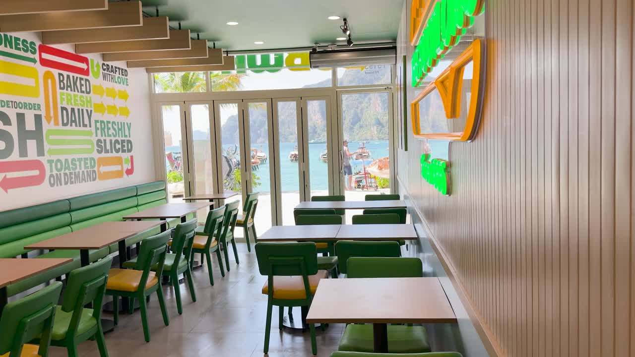 Un addetto in divisa lava il pavimento di un ristorante luminoso con vista su un oceano tropicale.
