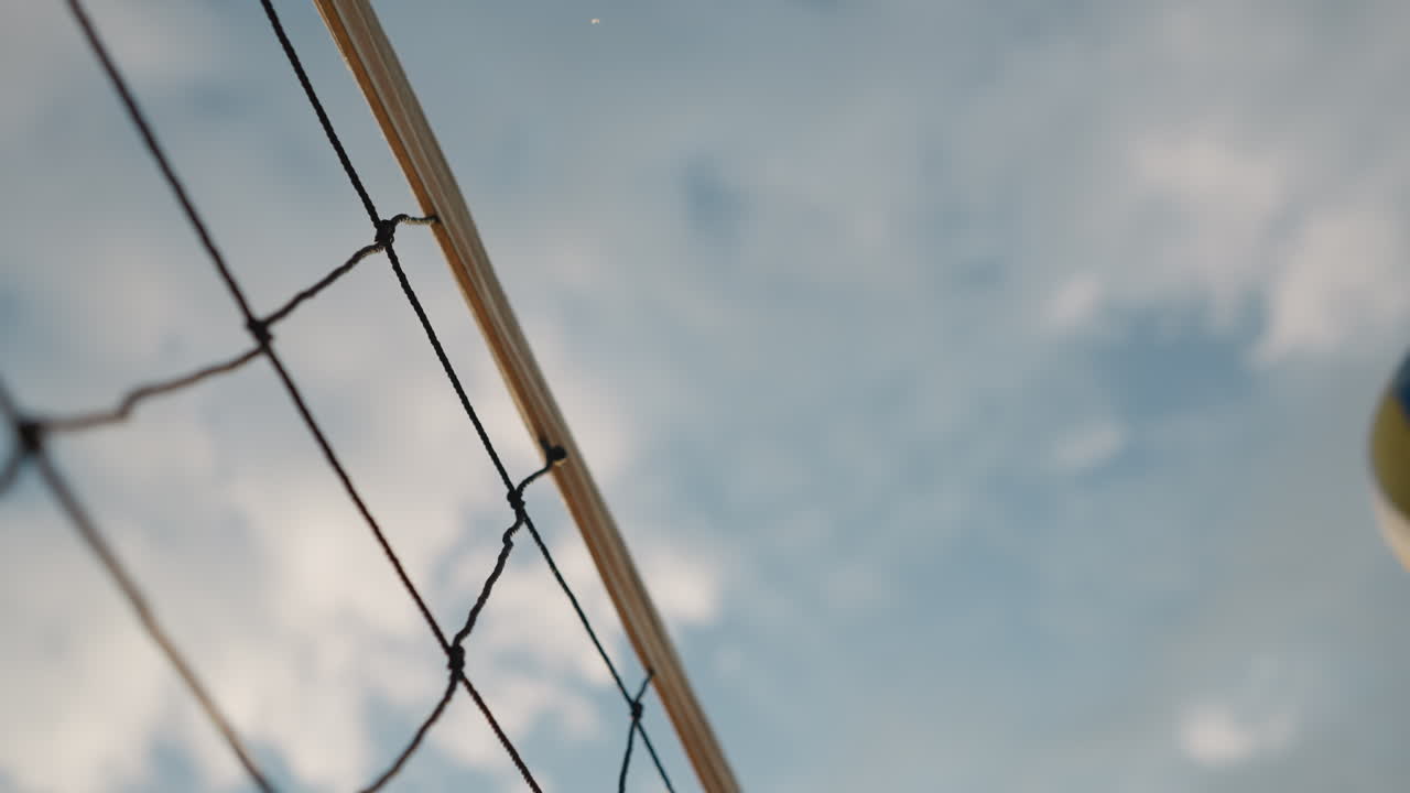 밝은 하늘 아래에서 볼이 놀고 있는 배구망의 클로즈업, 아름다운 자연 배경으로 야외 배구 경기에서 흥미진진한 순간을 포착합니다.