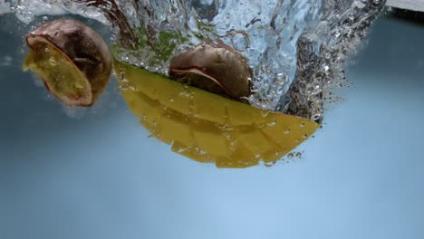 mango y fruta de la pasión cayendo en el agua en cámara súper lenta con fondo azul