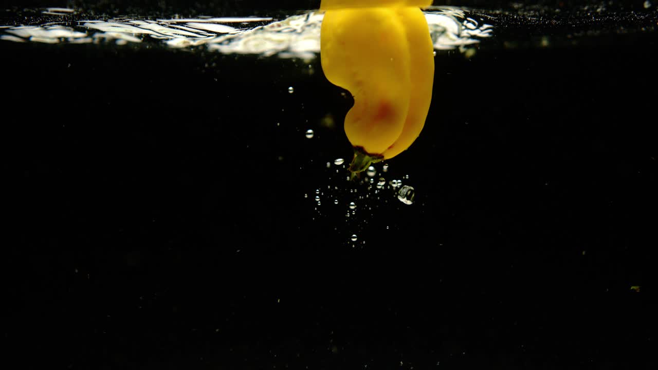 검은 바탕에 물에 떨어지는 신선한 마담 제네트 고추의 슈퍼 느린 움직임