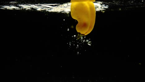 super slow motion of fresh madame jeanette peppers falling into water on black background