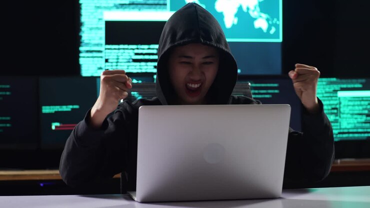 Asian Female Hacker In A Hood Celebrating Succeed Attack Global Infrastructure Servers By A Laptop With Maps And Data On Display Screens Of Multiple Monitors In A Dark Office Room