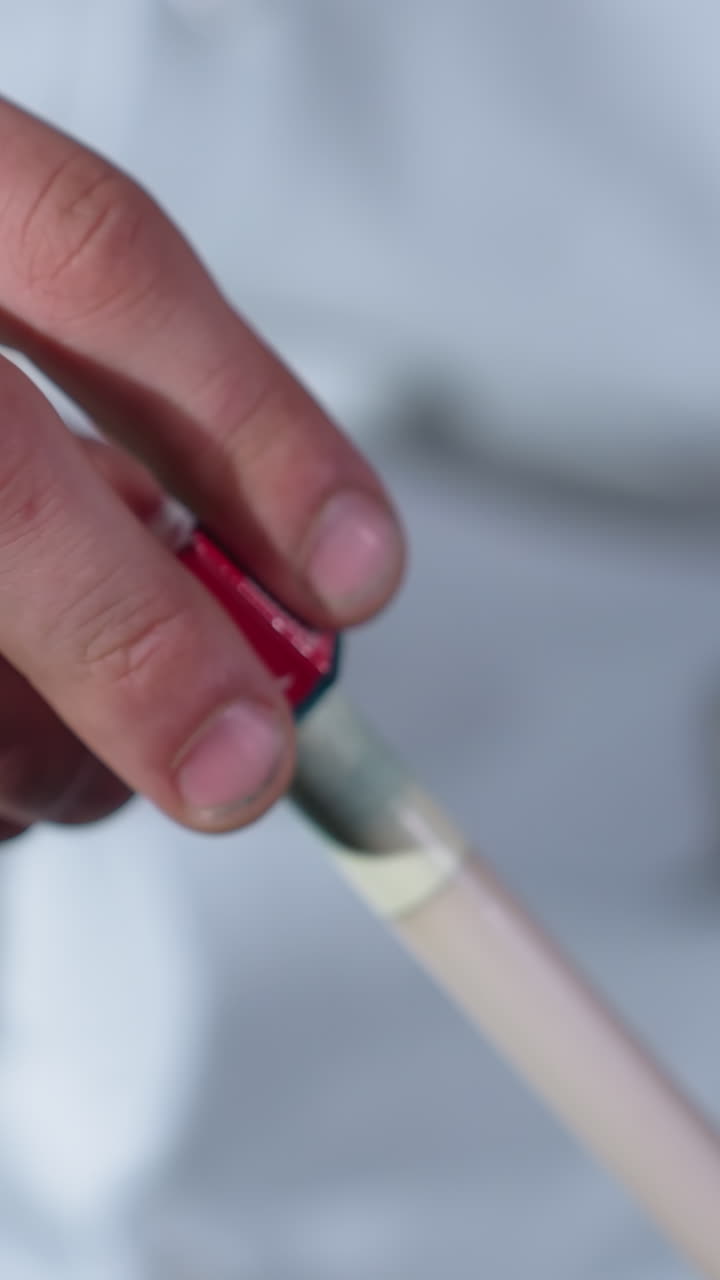 toma de primer plano de la mano con camisa blanca aplicando cuidadosamente la tiza al palo de señal antes del juego de billar. el agarre enfocado y el fondo borroso destacan la preparación, la precisión y la habilidad en el billar