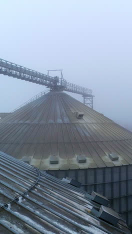 dirty roofs of elevator bins on misty weather. flying high between the metal tanks of agricultural plant. drone footage. vertical video