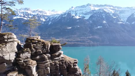 Vuelo-De-Drones-Sobre-Una-Roca-En-Un-Brillante-Lago-De-Montaña-Azul-Turquesa-En-Suiza