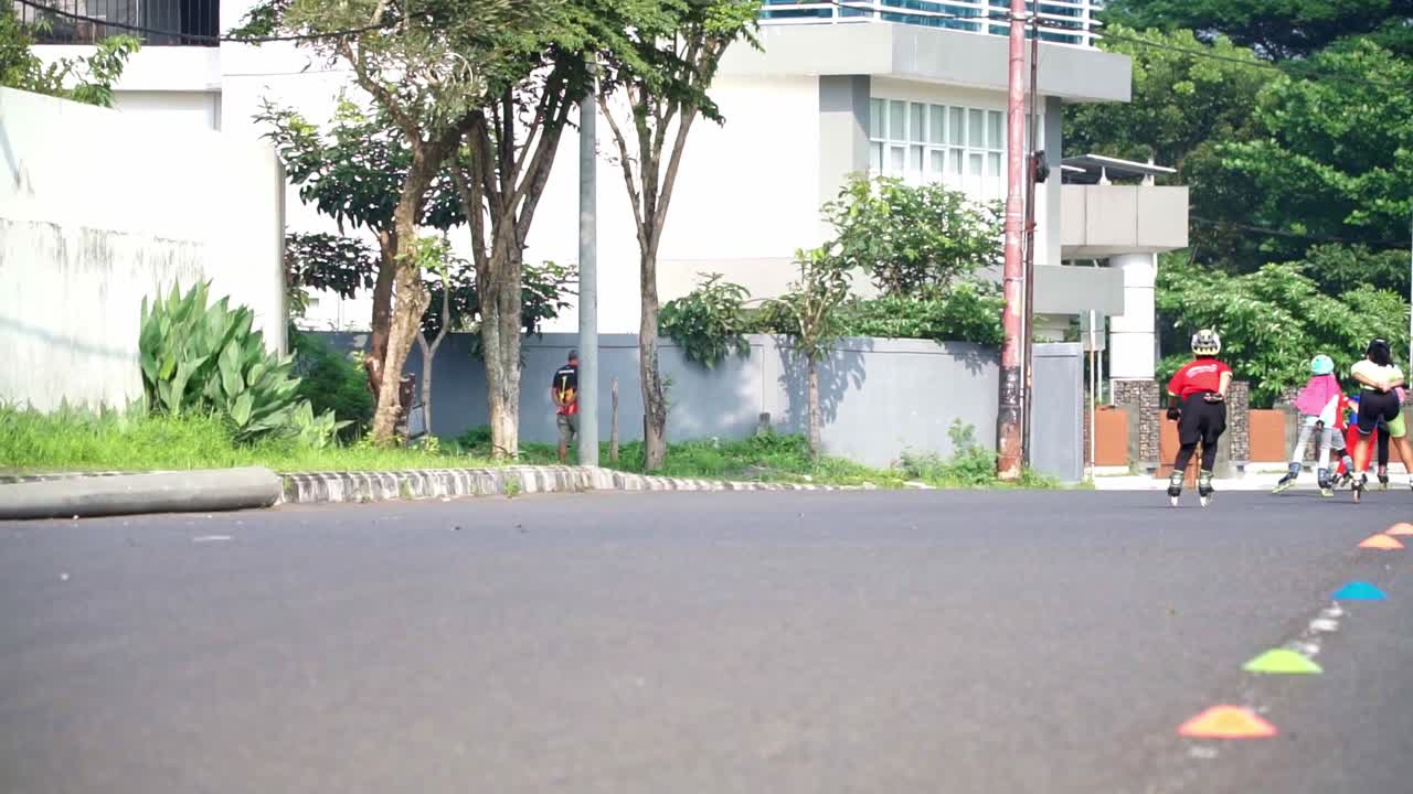 The camera records from behind a row of children speeding along on roller skates on a paved track.