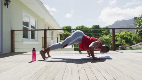 Focused-biracial-man-practicing-yoga-on-mat-on-terrace