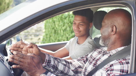 happy african american father instructing smiling son in car before driving lesson, slow motion