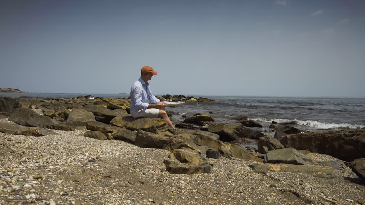 Man sitting on rocks by sea shore on a lovely sunny day, skimming stones into the sea off Cala De Mijas Beach