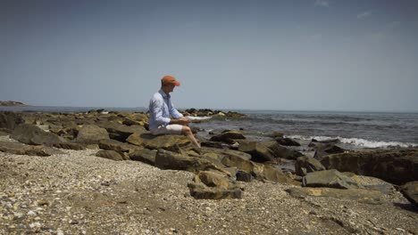 man sitting on rocks by sea shore on a lovely sunny day, skimming stones into the sea off cala de mijas beach
