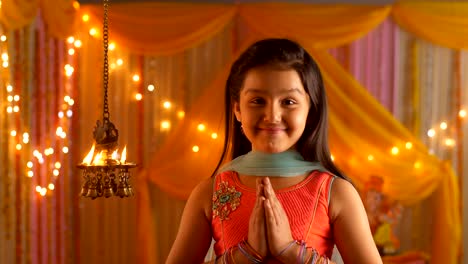indian girl with a smiling face looking at diyas - folding hands in namaskar position - greeting pose