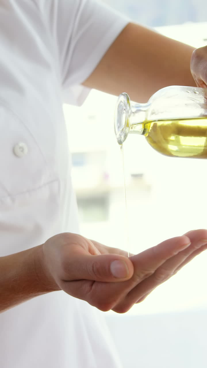 Masseur pouring massage oil in her hands