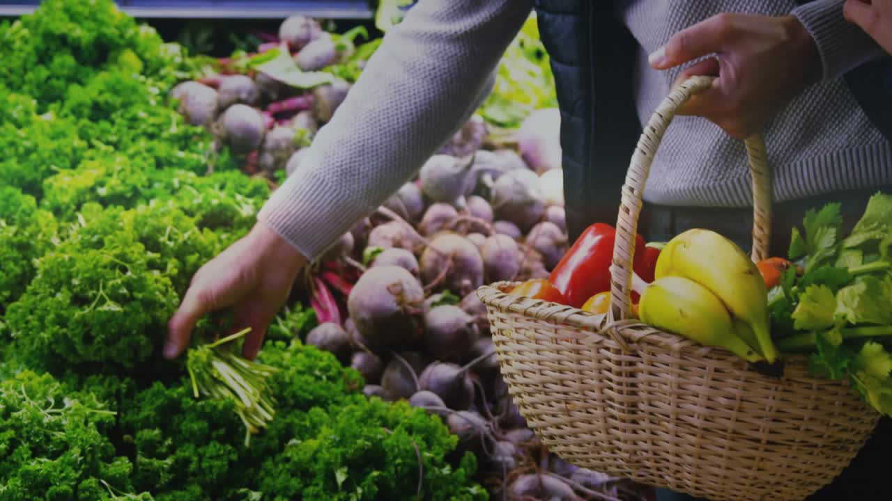 Woman shopper reaching, choosing greens in produce, partner holding basket, touching arm, shopping