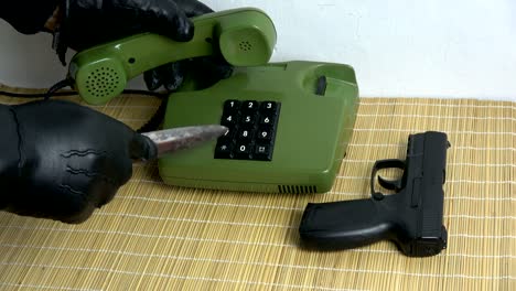 robber gangster hand with glove and dagger gun  pressing numbers buttons on retro telephone