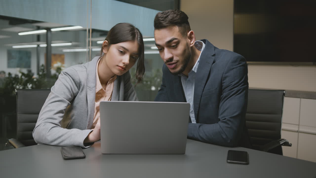 Two business professionals collaborating on a laptop in an office