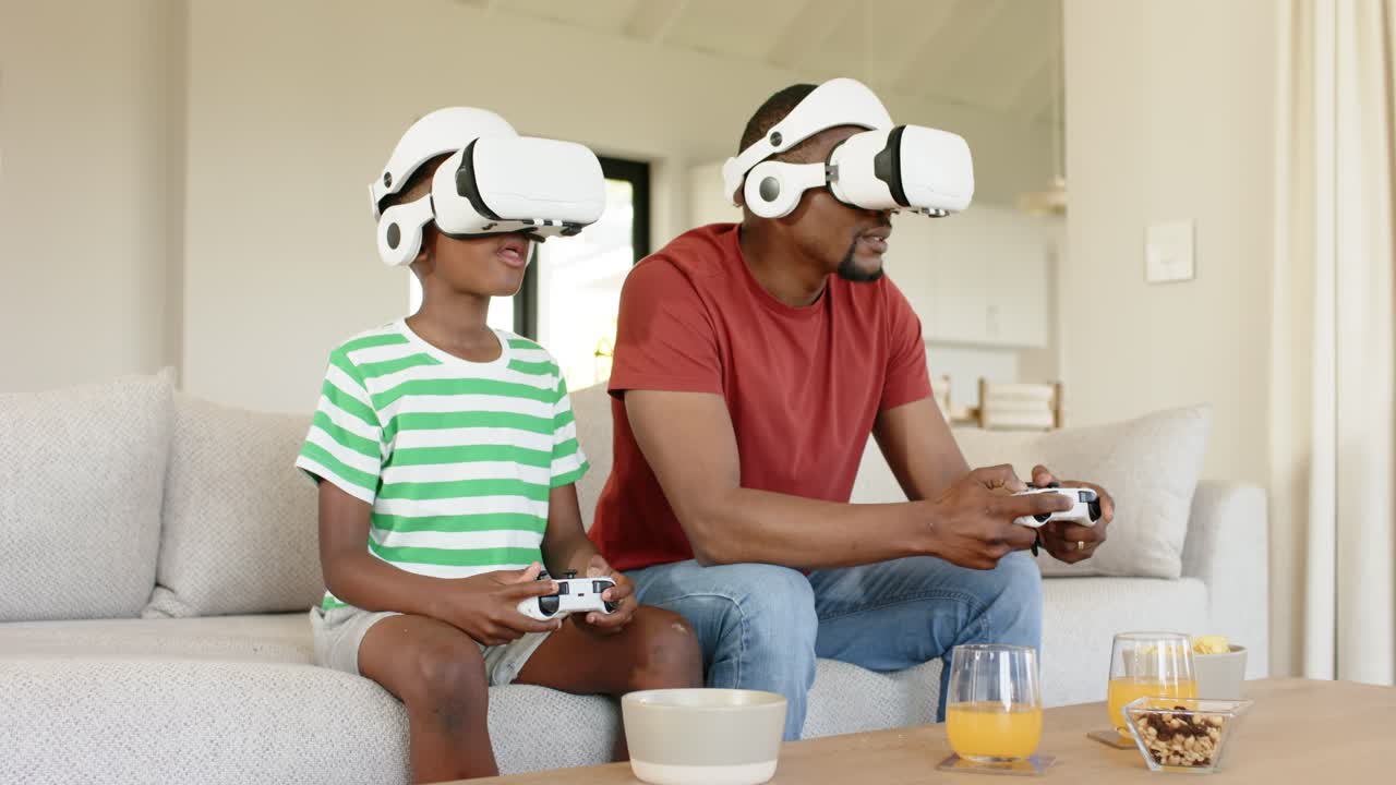 Padre e figlio afroamericani che indossano visori VR bianchi e si divertono a casa toccando i controller