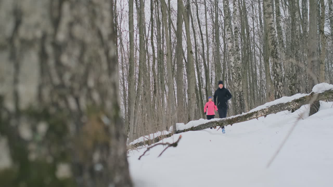 una pareja joven y saludable, positiva y hermosa, corriendo con ropa deportiva por el bosque en la soleada mañana de invierno. salta sobre el árbol, supera las dificultades del camino. pasar por encima de un obstáculo
