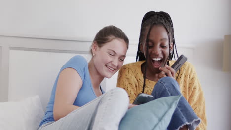 felices amigas adolescentes diversas acostadas en la cama usando teléfonos inteligentes y riendo