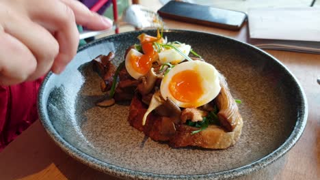 person eating perfectly cooked poached eggs on sourdough bread with mushrooms for breakfast in a local cafe, close up of delicious brunch of eggs on toast