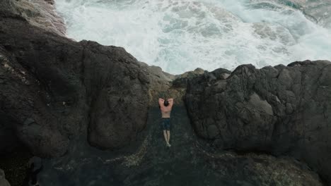 top-down aerial of a man floating peacefully in volcanic tide pools near crashing ocean waves in seixal, madeira.