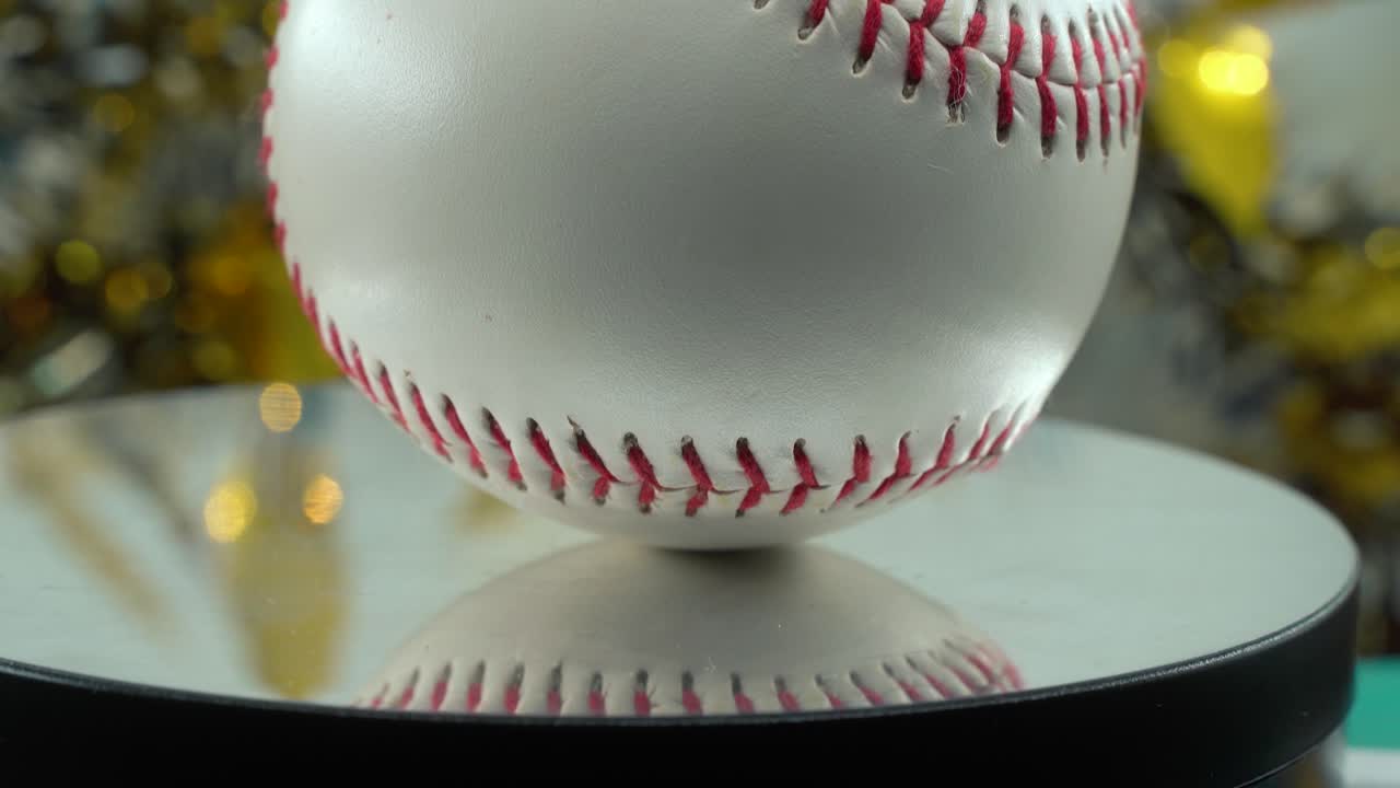 fotografía cinematográfica lenta de un primer plano de una pelota de base blanca, puntos rojos, béisbol en un soporte brillante, decoraciones navideñas borrosas en el fondo, iluminación de estudio profesional, panela de video 4k a la derecha
