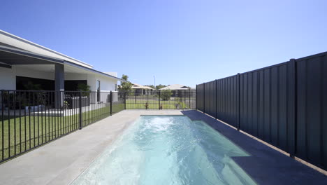 large luxurious contemporary outdoor swimming pool in ground, clear blue water black fence grey tiled decking close up of pool spa modern home green grass blue skies