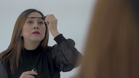 Woman-with-brown-hair-applying-mascara-to-eyelashes-using-large-mirror