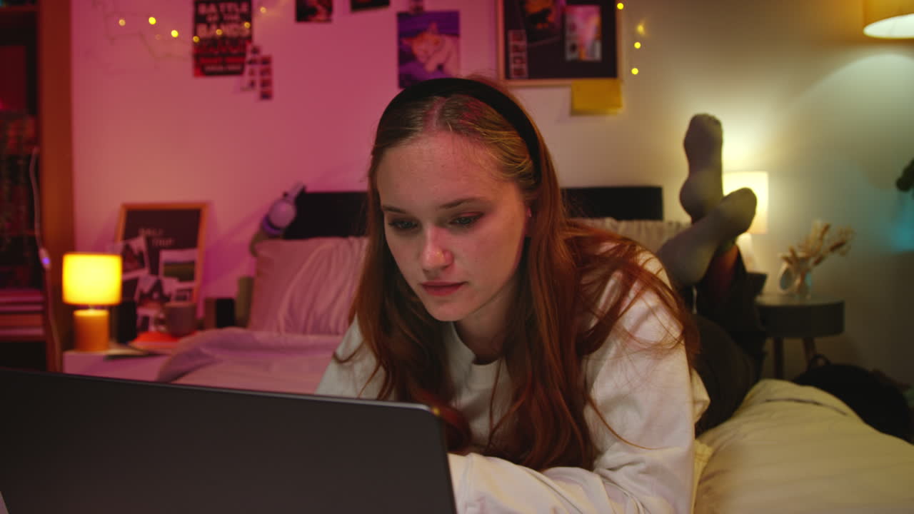 A young woman in a bedroom relaxing and using a laptop