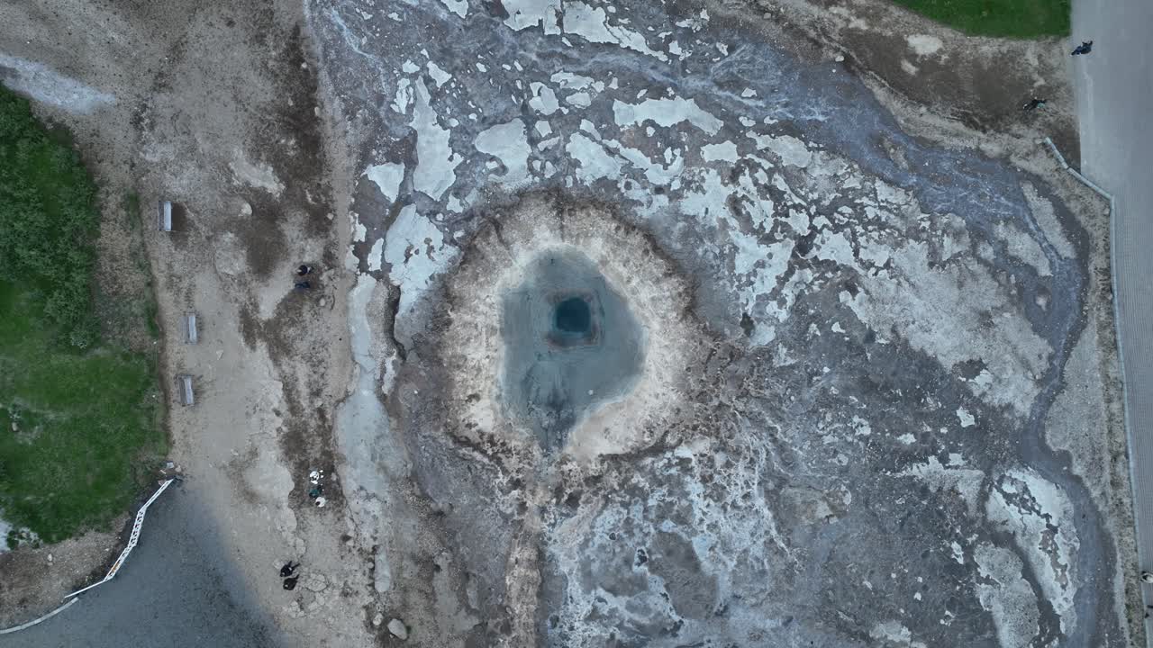 un dron disparado directamente por encima de geysir en islandia capturando una erupción con vapor y agua que se eleva desde el cráter geotérmico en un paisaje accidentado.