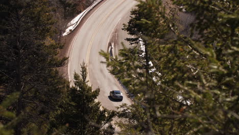 cars drive along a winding mountain road in the forest, long lens