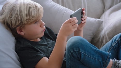 happy little boy using smartphone playing game relaxing on sofa at home child browsing online with mobile phone technology anti social addiction concept 4k footage