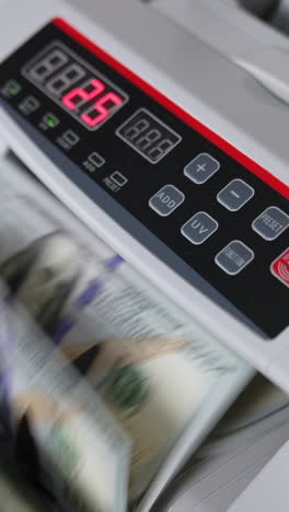 male hand inserts a wad of hundred dollar bills into a slot of cash counting machine. equipment for financial operations close up. blurred backdrop. vertical video