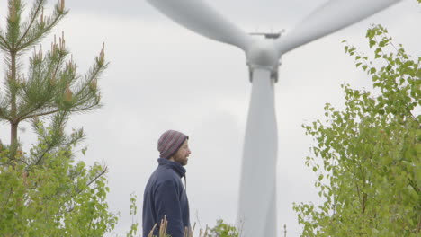 a 40 year old man pauses during a walk to look at the huge wind turbine in front