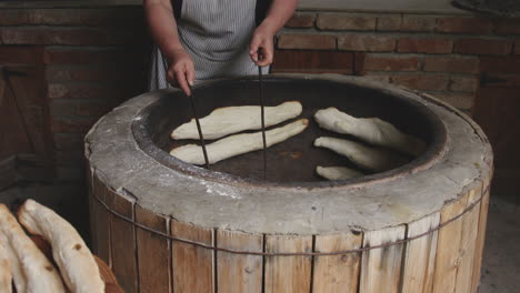 woman removing georgian shotis puri bread sticking on the stone wall of tone oven