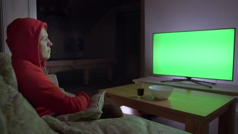 a man in a hood watches the news on tv and switches channels with a remote control, sits on the couch, chroma key