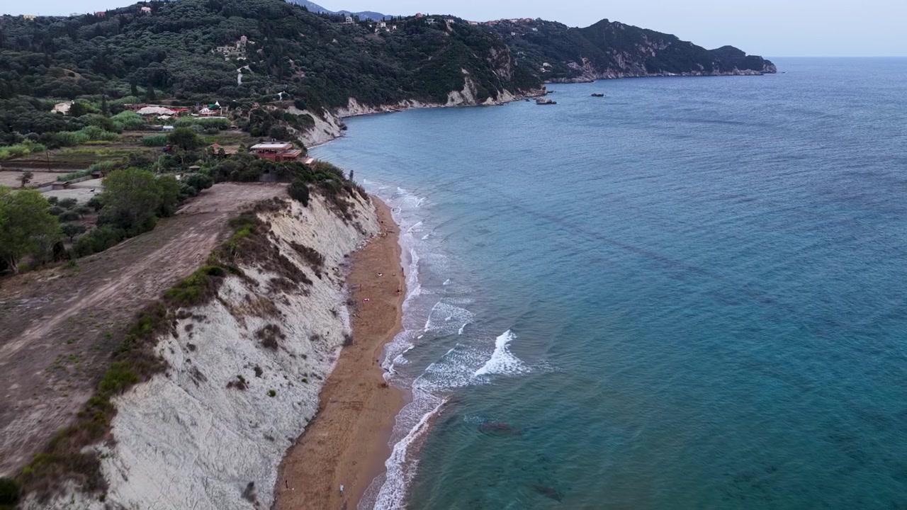 Aerial drone view of majestic clay cliffs and sandy Arillas beach on the Ionian Sea coastline, lush green hills and turquoise water in Corfu Greece summer trip
