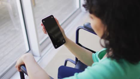 mujer discapacitada biracial en silla de ruedas usando un teléfono inteligente en la sala de estar, copia el espacio en la pantalla