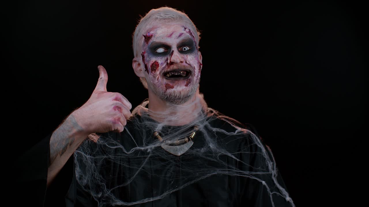 Sinister man Halloween zombie raises thumbs up agrees with something or gives positive reply, likes