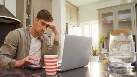 Worried-man-using-his-calculator-while-working-on-laptop-4K-4k