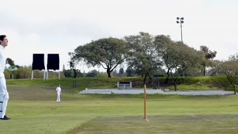 two teams of multiracial male cricket players and male umpire playing cricket on pitch