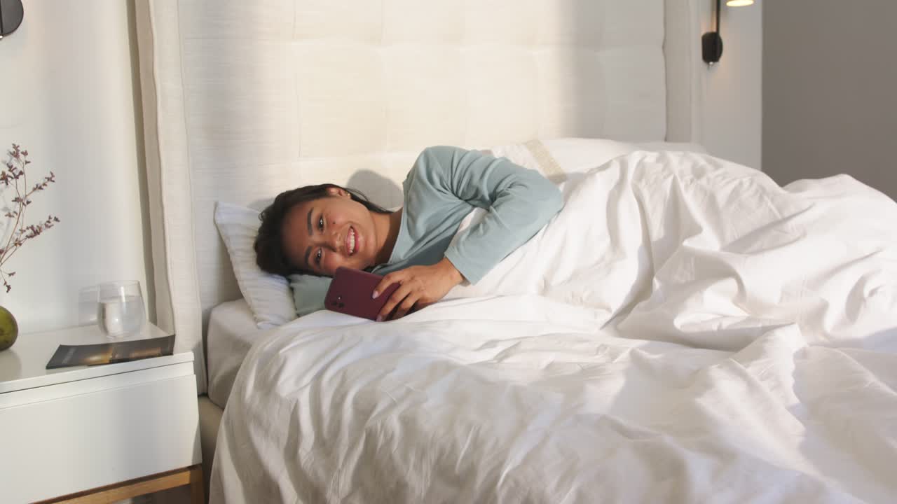 Wanita Asia paruh baya di tempat tidur menatap, menggulir ponsel pintar untuk membaca pesan sambil tersenyum di bawah selimut.