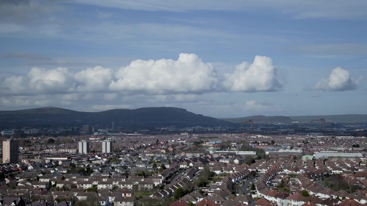Bred telezoom timelapse af Belfasts bysilhuet i Nordirland med bevægende skyer, trafikstrøm og havnekraner set fra Rocky Road om dagen.
