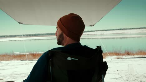 a millennial male overlooks a gorgeous winter lake underneath a camping awning