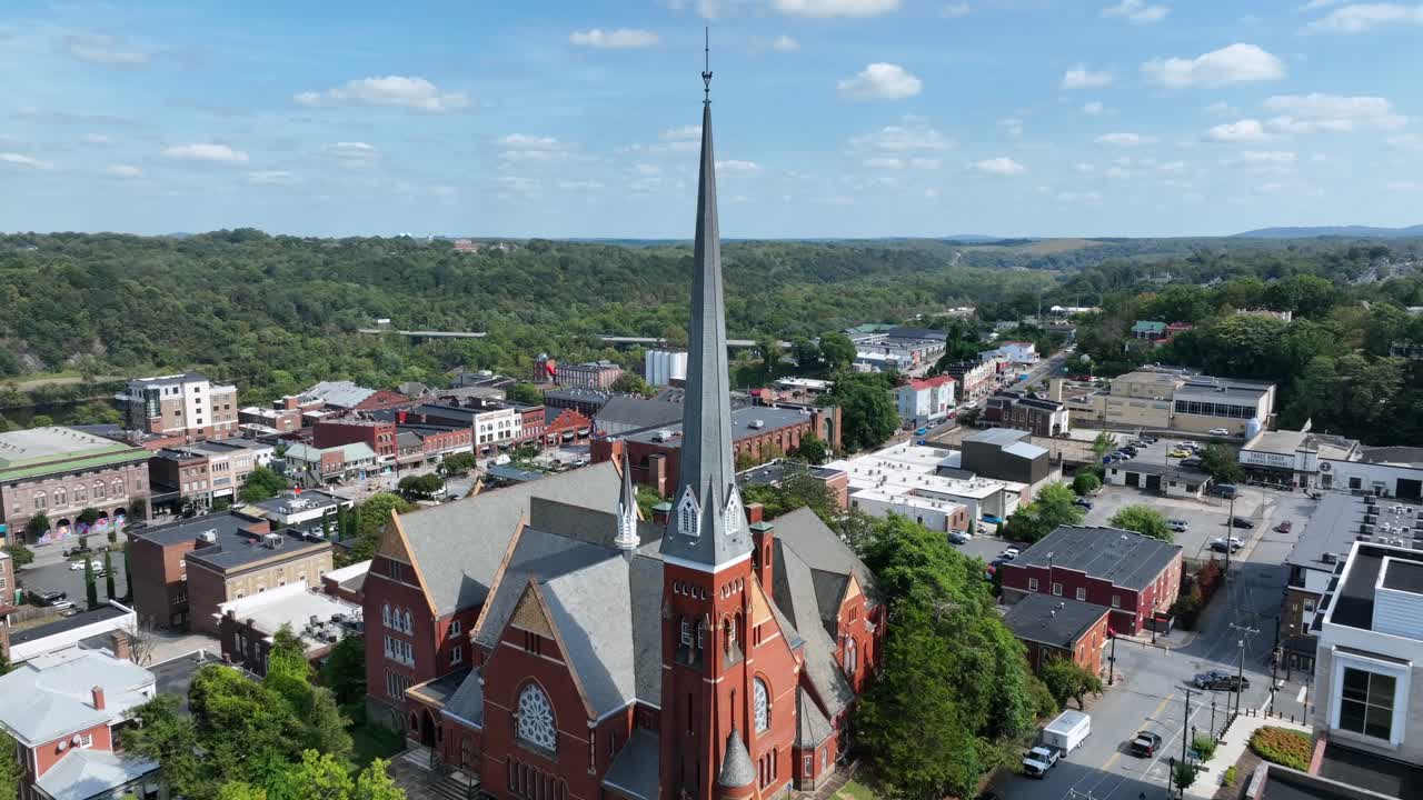 Aerial approaching shot of red brick church with tower in downtown of small American town. Sunny day in fall season. Traffic on suburb highway in distance. Wide shot